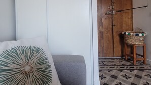 A room with a grey sofa, a white wall, a wooden door, and a patterned floor. - Beautifully located studio in the heart of the village, renovated (Brando)