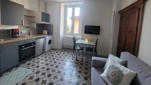 A compact kitchen with a washing machine, a coffee maker, and a dining area with a table and chairs. - Beautifully located studio in the heart of the village, renovated (Brando)