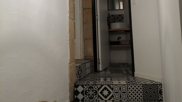 Un pasillo con baldosas estampadas, una puerta que da a una habitación y un candelabro colgante.