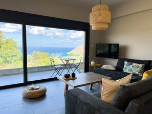 Una sala de estar moderna con un gran ventanal corredera que da a un balcón con vistas al mar.