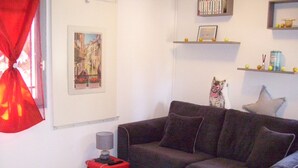 Un salon avec un canapé foncé, une petite table d’appoint avec une lampe, un tableau encadré au mur et une statuette de chat.