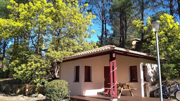 Un petit bâtiment avec un toit en tuiles, une terrasse en bois et un vélo garé à proximité.