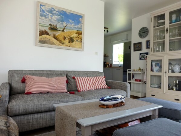 A living room with a grey sofa, striped cushions, a coffee table with a bowl, and a painting of a beach scene.