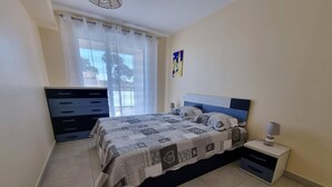 Ein Schlafzimmer mit Bett, Kommode, Nachttisch und einem Fenster mit Vorhängen.