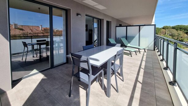 Ein moderner Balkon mit Esstisch und Stühlen, großen Schiebeglasfenstern und Blick auf die Stadtlandschaft.