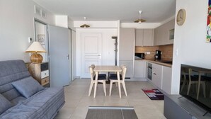 Eine moderne Wohnung mit einem grauen Sofa, einem Holzesstisch, einer Küche mit weißen Schränken und einem Fernseher auf der rechten Seite.