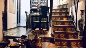 Een trap met decoratieve leuningen, een tafel met theepot en kopjes, en een eetgedeelte met stoelen en een tafelkleed.