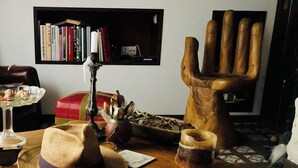 Een houten tafel met een hoed, een kaars, een decoratief handbeeld en een schaal met noten.