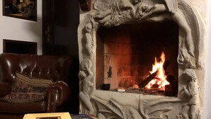 A fireplace with a stone surround, a leather armchair, and a table with books. - Cozy House Sleeps 2 With Pet Friendly Option (Portimão)