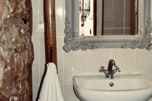 Un baño con un lavabo blanco, un espejo con detalles ornamentales y una toalla colgada en un perchero de madera.