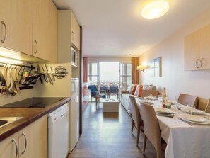 A modern hotel room with a kitchenette, dining area, and a balcony with a view.