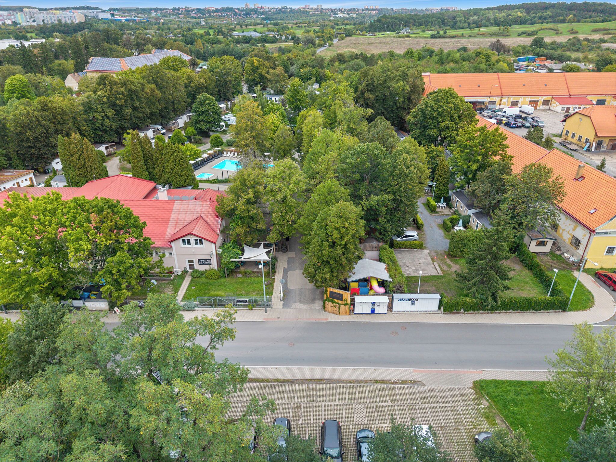 Ett flygbildsbild av ett bostadsområde med hus, en swimmingpool och en liten byggnad med ett rött tak.