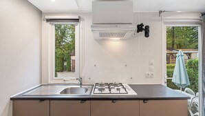Une cuisine de taille réduite, équipée d’une cuisinière à gaz, d’un évier et d’une fenêtre donnant sur un jardin.