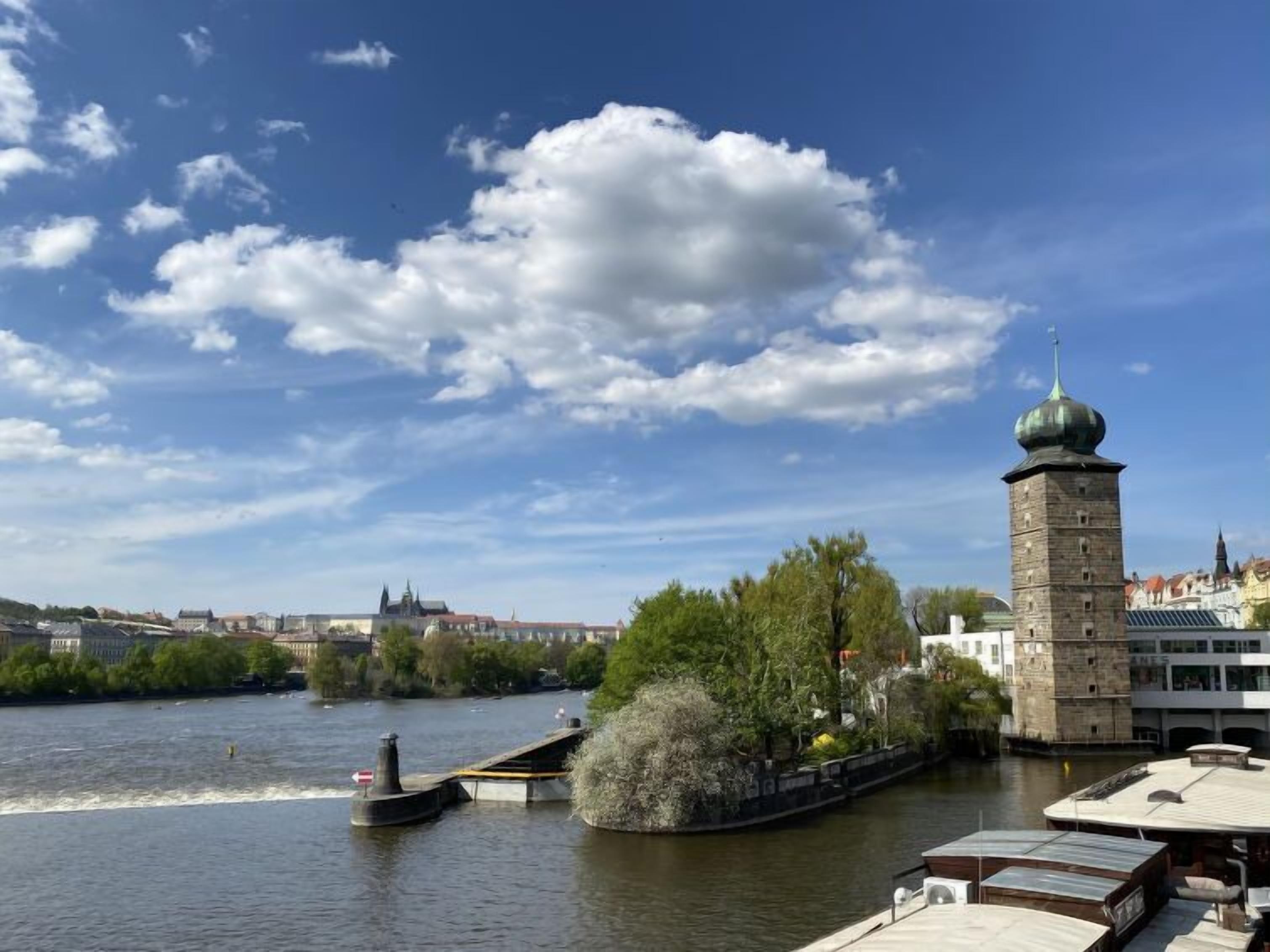 A riverside view with a tower and buildings in the background.