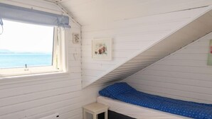 A small, white, attic-style bedroom with a single bed, a small stool, and a window overlooking a body of water. - Villa Hjartnes by Interhome (Baldersheim)
