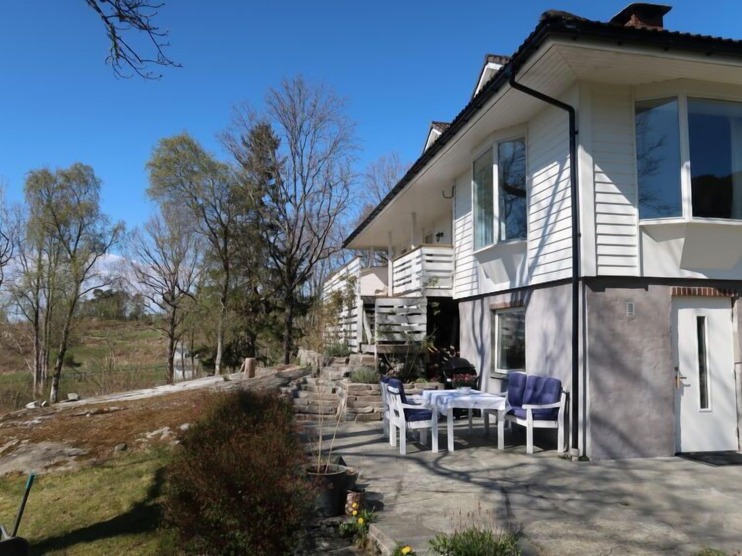 Ein zweigeschossiges Haus mit einem Balkon, einer Terrasse mit Gartenmöbeln und einem Kiesweg, der zum Eingang führt.