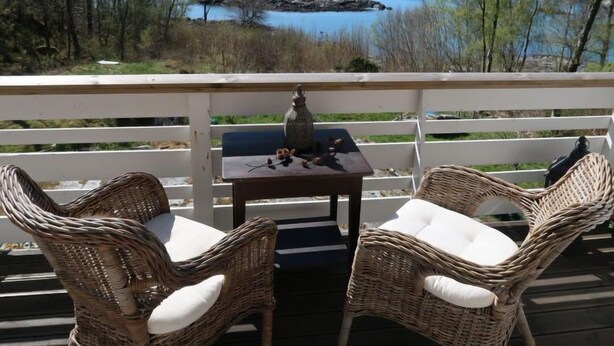 A deck with wicker chairs and a table, overlooking a lake with a rocky island and trees. - Villa Hjartnes by Interhome (Baldersheim)
