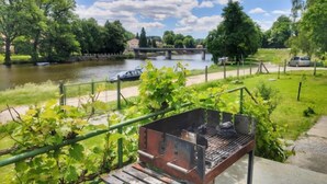 Vista al río con zona de parrilla, un puente y vegetación.