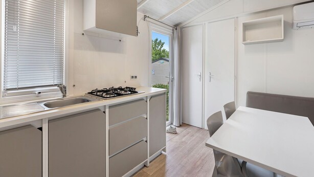 Una cocina moderna con estufa a gas, un lavamanos y una ventana con persianas. Hay una zona de comedor con una mesa y sillas.