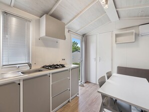 A modern kitchen with a gas stove, a sink, and a window with blinds. There is a dining area with a table and chairs.