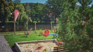 Un parque infantil con zona de juegos de arena, columpios y un banco.