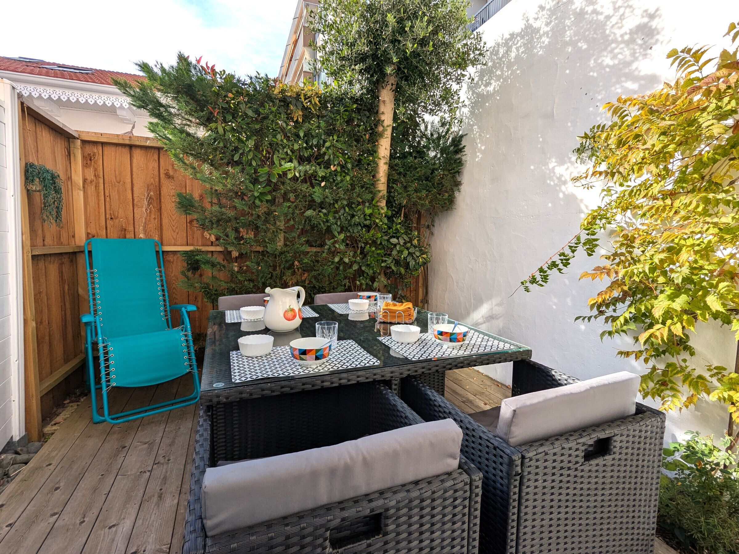 Une terrasse avec une table dressée pour quatre personnes, entourée de meubles en osier et d’une clôture en bois.