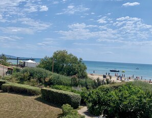 A beach with people, boats, and a lighthouse in the background.
