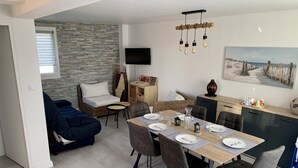 Ein modernes Wohnzimmer mit Sofa, Esstisch und Fernseher.