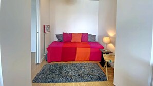 A bedroom with a bed, a bedside table, a lamp, a rug, and a picture on the wall. - Larmor-Plage 1BR with Terrace and Garage (Larmor-Plage)