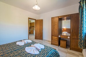 Una camera da letto con un letto, un'armadiatura in legno, una piccola scrivania con uno specchio e un bagno visibile attraverso una porta aperta.