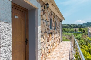 A stone building with a wooden door marked '18', a stone wall, and a metal railing overlooking a green landscape.
