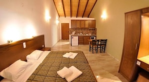 A bedroom with a bed, a small kitchenette, and a wooden wardrobe.