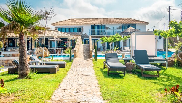 Un espace aménagé au bord de la piscine, avec des chaises longues, un chemin en pierre et un bâtiment doté d’un toit en tuiles.