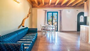 A room with a wooden ceiling, a blue patterned sofa, a dining table with chairs, and a view through a doorway. - Pet-Friendly Apartment 'Mirage Arillas Maisonette B' with Sea View, Shared Pool & Wi-Fi (corfu)