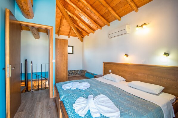 A hotel room with a wooden ceiling, a bed with a blue bedspread and white pillows, a wooden headboard, and a small window.