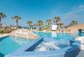 A swimming pool with a hot tub, surrounded by palm trees and a stone wall.
