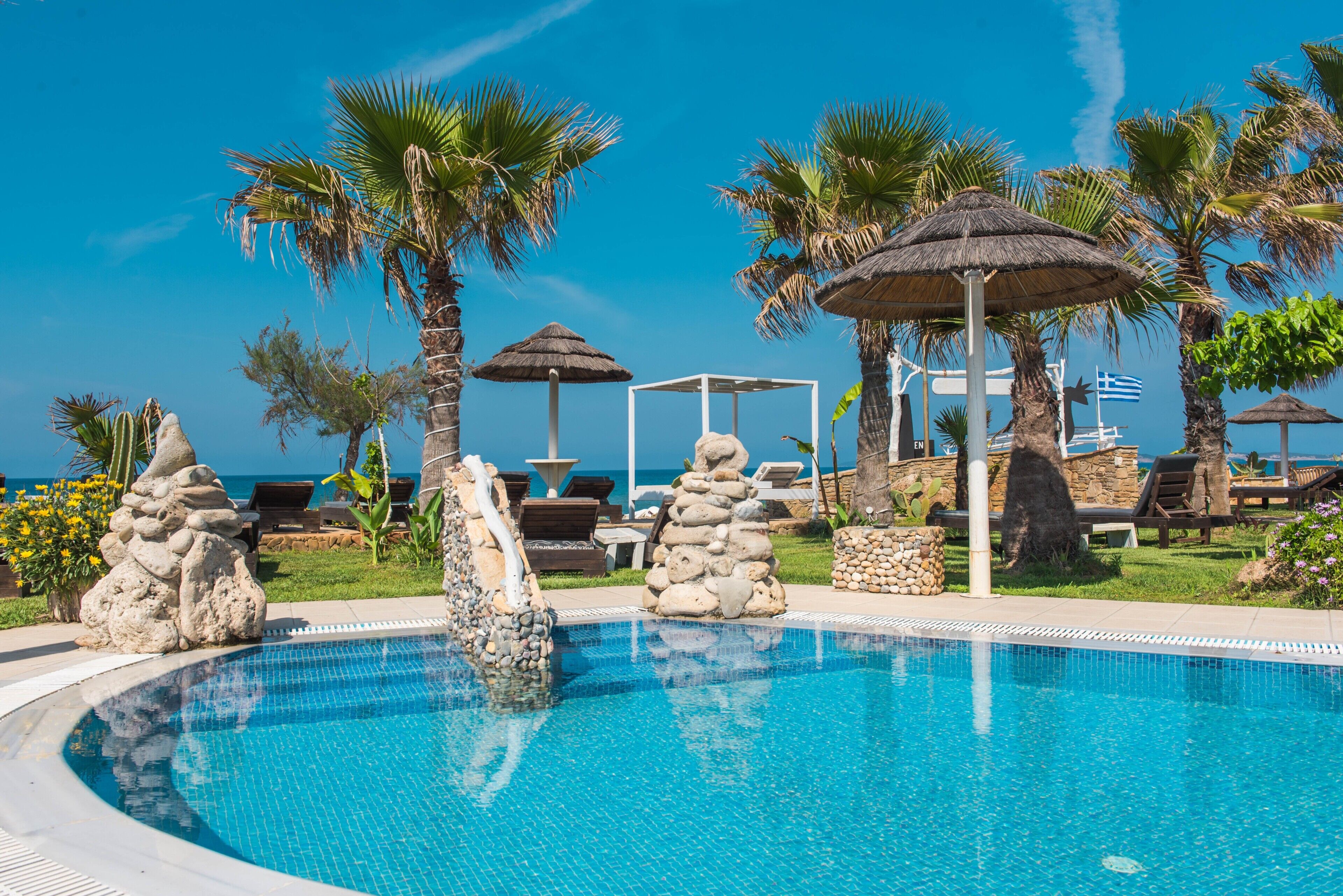 A pool with clear blue water, surrounded by palm trees, lounge chairs, and a gazebo.