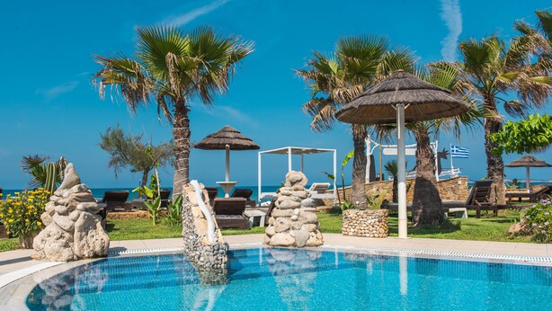 Ein Pool mit klarem, blauem Wasser, umgeben von Palmen, Liegestühlen und einem Gazebo.