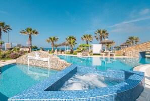 A swimming pool with a hot tub, surrounded by palm trees and a stone wall.