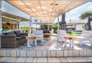 An outdoor patio with wicker furniture, a pool, and a covered area with a signboard.