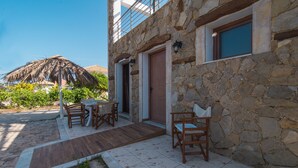 Ein Steinhaus mit Holztür, einem Balkon und einem reetgedeckten Sonnenschirm.
