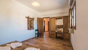 Ein Zimmer mit Holzboden, einem Bett mit weißen Bettwäsche, einem Sessel, einem Schreibtisch und einem Spiegel.