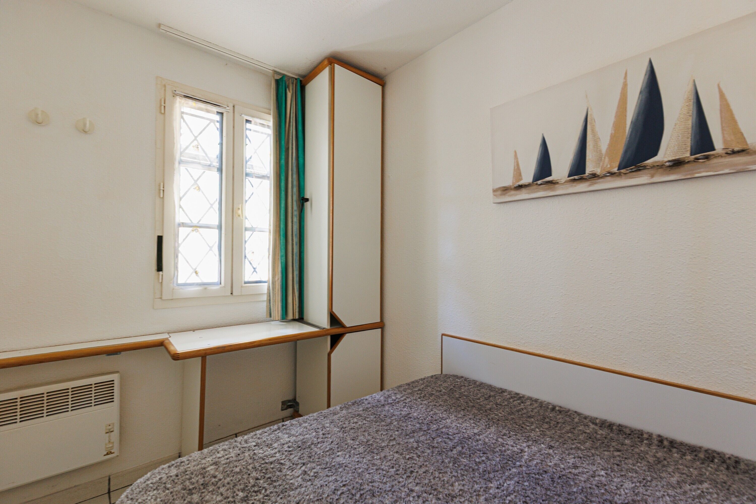 A room with a bed, a window with curtains, a radiator, and a wall-mounted artwork.