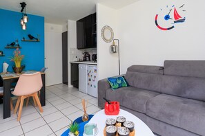 Ein modernes Wohnzimmer mit grauem Sofa, einem Essbereich mit Tisch und Stühlen, einer Küche mit schwarzen Schränken und einer Wanduhr.