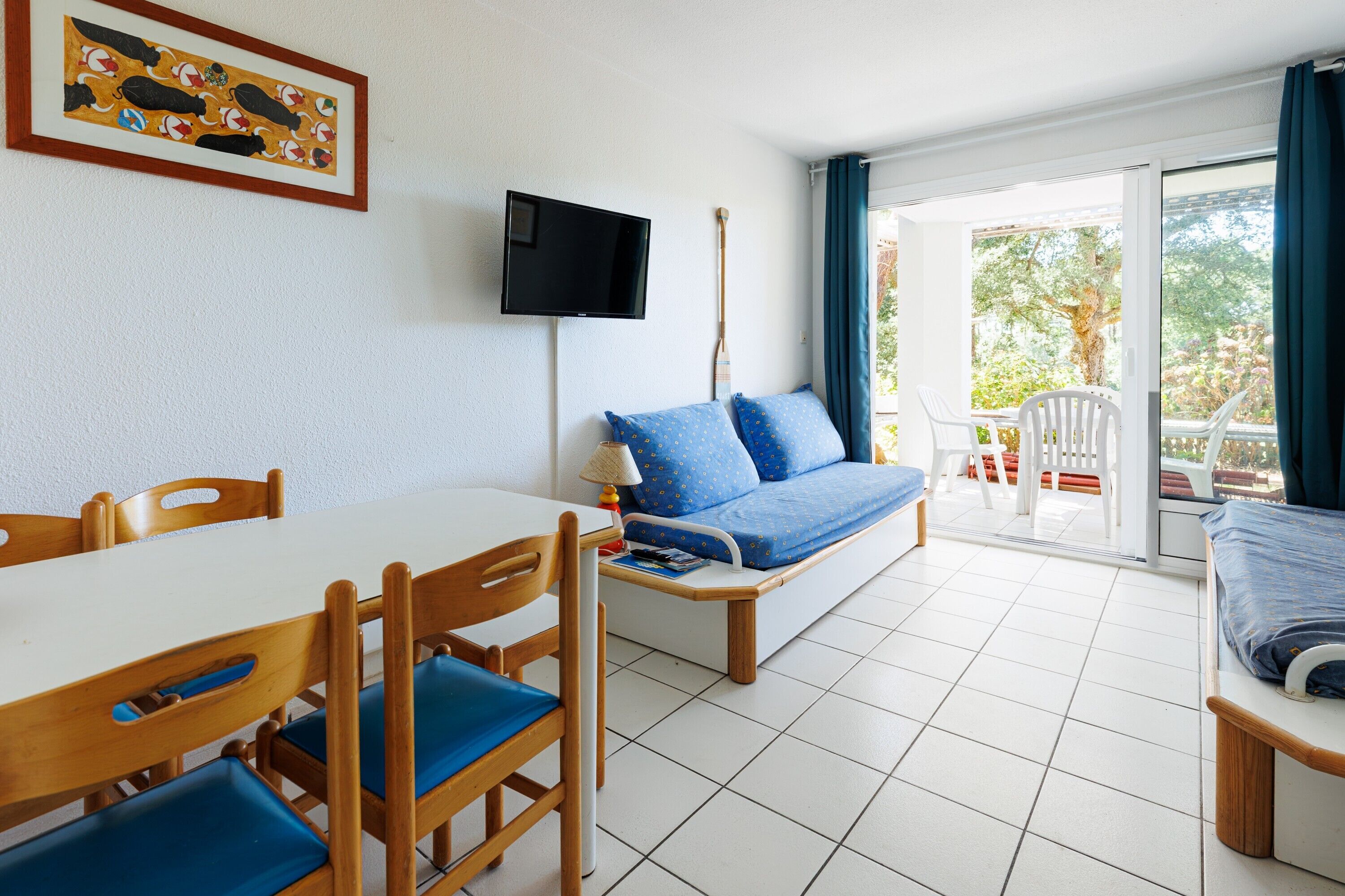 Une pièce comprenant une table à manger, des chaises, un canapé, un téléviseur et une vue sur l’extérieur, visible à travers une porte vitrée.