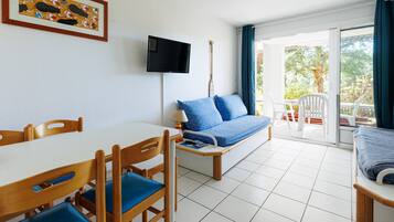 Une pièce comprenant une table à manger, des chaises, un canapé, un téléviseur et une vue sur l’extérieur, visible à travers une porte vitrée.