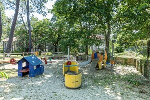 Une aire de jeux avec une maisonnette bleue, des jeux colorés en jaune et en bleu, et un toboggan.