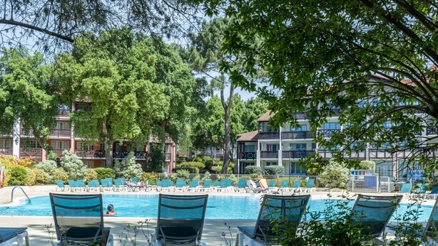A pool area with lounge chairs, a swimming pool, and a building with balconies in the background.