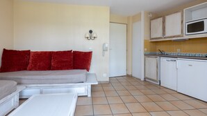 A compact living space with a sofa, a dining table, a kitchenette with a microwave, and a door leading to another room.