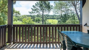A covered patio with a view of a green landscape, a table, and chairs.